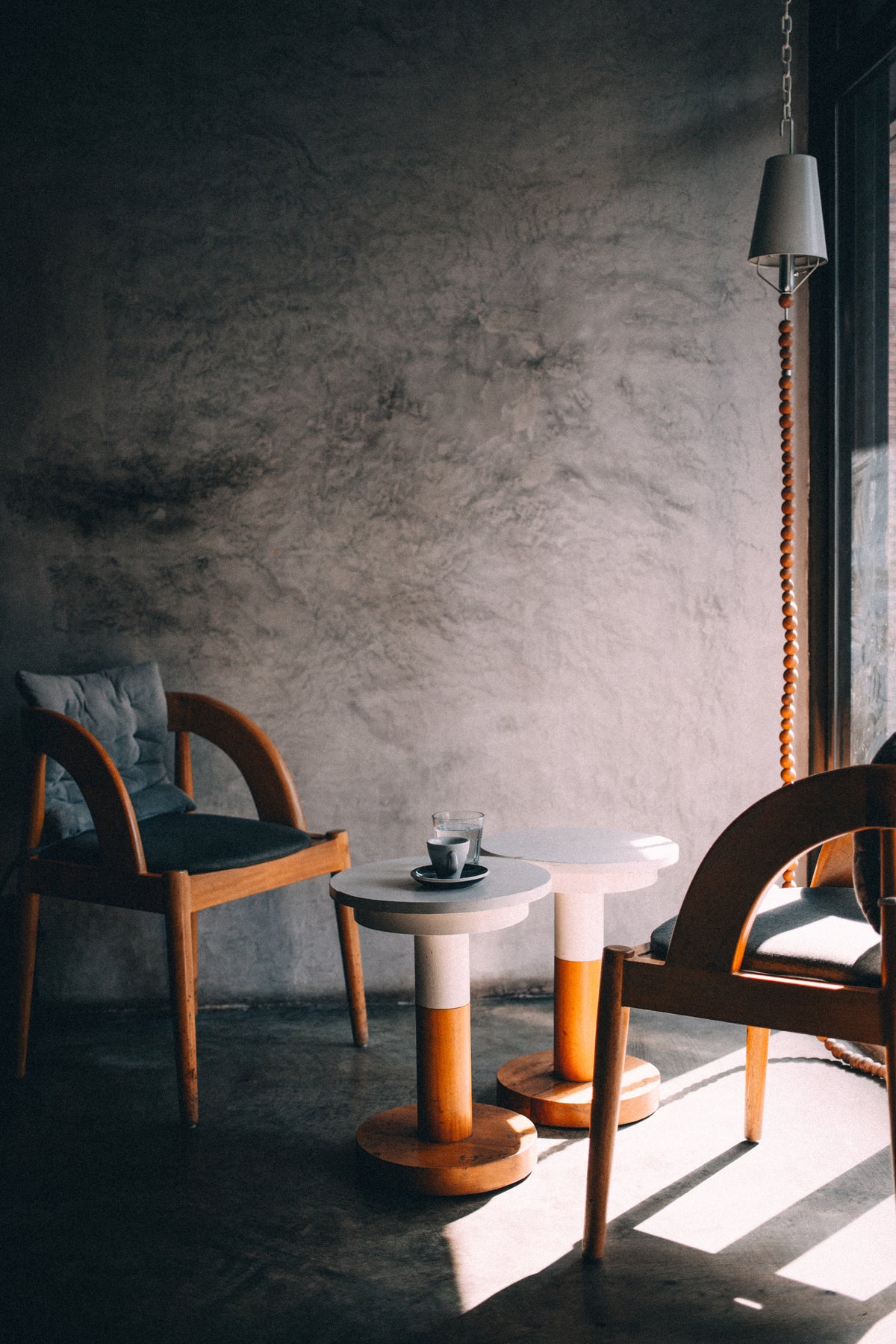 Two wooden chairs with a small round table against a textured gray wall.